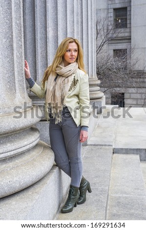 Dressing in a light green jacket, long beige scarf, tight gray fashion pants and green boots, a young pretty woman is standing by a column outside an office building / Portrait of Businesswoman