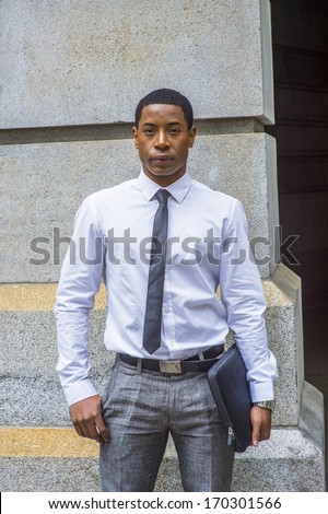 Dressing in white shirt, a black tie, gray pants, carrying a briefcase, a young handsome black college student is standing by a stone wall, confidently looking at you. / Portrait of a College Student