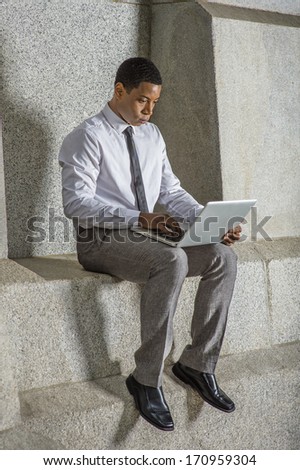 Dressing in white shirt, a black tie, gray pants and leather shoes, a young black college student is working on a computer outside / Working Outside