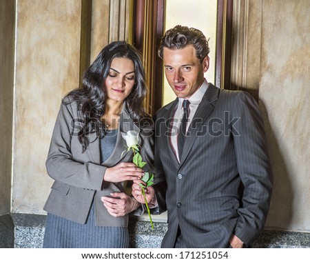 A young handsome businessman is giving a white flower to a pretty businesswoman by a small window / Love Between Businessman and Businesswoman