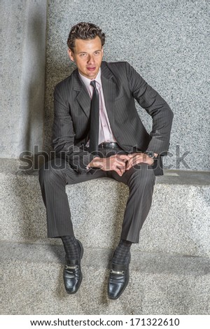 Dressing in a black striped jacket, tie, pants, leather shoes, wearing a watch, a hand and a arm resting on laps,  a young businessman is sitting outside, relaxing and thinking. / Relaxing Outside