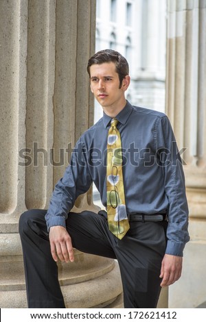 Dressing in a blue shirt, black pants, a colorful tie, one arm resting on one leg, a young college student is standing outside an office building, into deeply thinking. / Thinking Outside