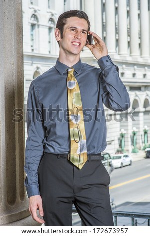 Dressing in a blue shirt, black pants, a colorful tie, a young college student is standing outside a business building, making a phone call. / Calling Outside