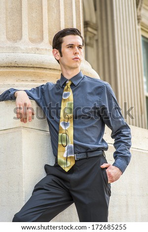 Dressing in a blue shirt, black pants, a colorful tie, a young college student is standing outside an office building, looking forward. / Portrait of College Student