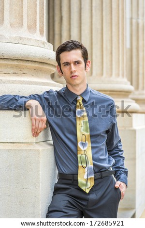 Dressing in a blue shirt, black pants, a colorful tie, a young college student is standing outside an office building, thinking. / Portrait of College Student