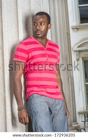 Dressing in red, pink stripe Henley V Neck T shirt,  gray pants, wearing a bracelet, a young black guy is standing by a pillar, confidently looking forward. / Portrait of Young Black Guy
