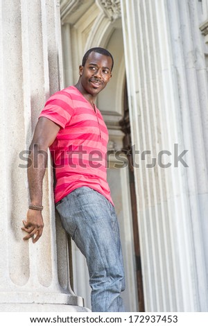 Dressing in red, pink stripe Henley V Neck T shirt,  gray pants, wearing a bracelet, a young black guy is standing by a column, smiling and waiting for you. /Waiting for You