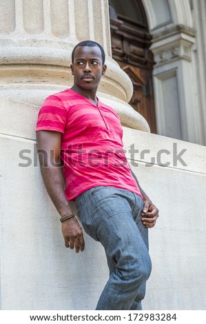 Dressing in red, pink stripe Henley V Neck T shirt,  gray pants, wearing a bracelet, a young black guy is standing against the base of a column  outside an office, waiting for you. / Young Black Guy