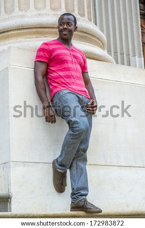 Wearing a red, pink stripe Henley V Neck T shirt,  gray pants, leather sneakers, a young black guy is standing against the base of a column, smiling and waiting for you. / Portrait of Young Black Guy