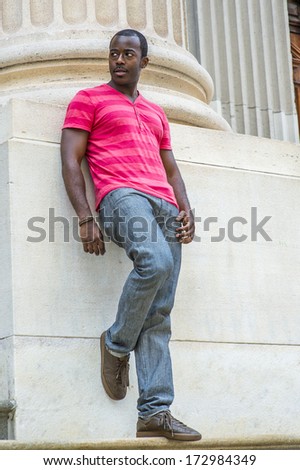 Wearing a red, pink stripe Henley V Neck T shirt,  gray pants, leather sneakers, a young black guy is standing against the base of a column, bending over a leg, waiting for you. / Waiting for You.