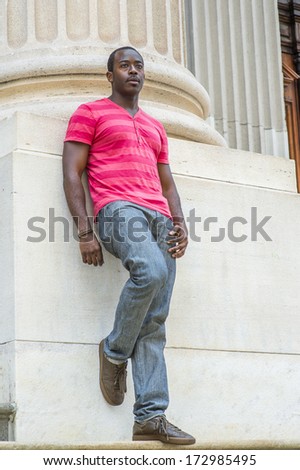 Wearing a red, pink stripe Henley V Neck T shirt,  gray pants, leather sneakers, a young black guy is standing against the base of a column, relaxing and thinking. / Relaxing and Thinking Outside