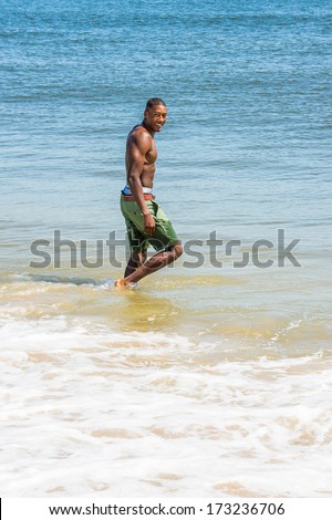 A well built young sexy black guy, half naked,  is walking on water of ocean, turning back, smiling. / Wading on Beach