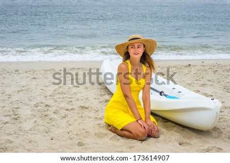 Wearing a bright yellow sundress, a straw hat,  a pretty girl is kneeling down on the beach by a small white lifeguard boat, relaxing / Beach Vacation