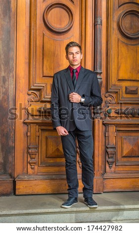 Dressing in a red undershirt, a black blazer,  jeans,  tie, leather sneaker,  a handsome college student is standing in the front of old fashion style door, looking forward. / Portrait of Student