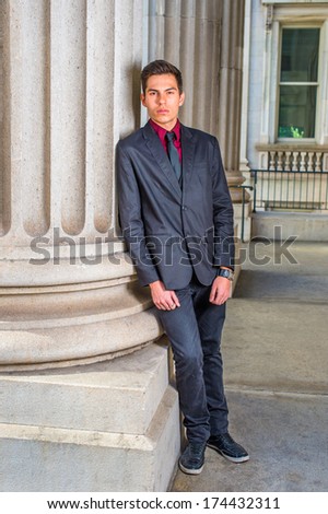 Dressing in a red undershirt, a black blazer, black jeans and a black tie, a college student is leaning against a column outside a office on the campus, relaxing and thinking. / Relaxing Outside