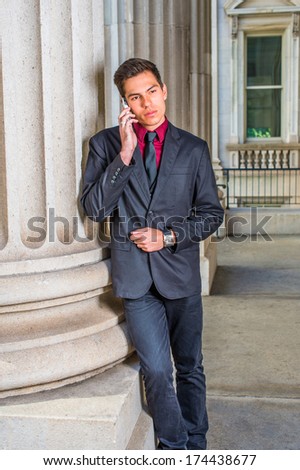 Dressing in a red undershirt, a black blazer,  jeans,  tie, a young handsome college student is leaning against a column outside an office, making a phone call. / Calling Outside