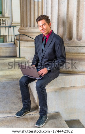 Dressing in a red undershirt, a black blazer, jeans, a black tie, a young college student is working on a laptop computer outside an office on campus. / Studying Outside