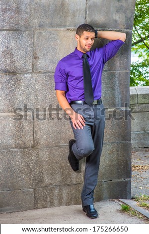 Dressing in purple shirt, gray pants, black tie, leather shoes, one hand putting in the back of his head, one foot touching the wall, a college student is standing by the wall, frowned, thinking.