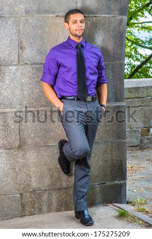 Dressing in a purple shirt, gray pants, a black tie, leather shoes, two hands putting in pockets, one foot touching the wall, a young businessman is leaning against the wall, relaxing outside.