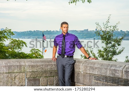 Dressing in a purple shirt, gray pants and a black tie, a young handsome lawyer with a little beard and mustache is standing by a river, confidently looking forward. / Portrait of Young Handsome Guy