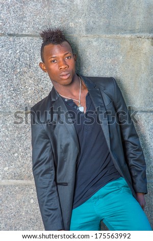 Dressing in a black blazer, green pants, a young black guy with mohawk hair is leaning against the wall, his body tilted one side, confidently looking at you. / Portrait of Young Black Guy