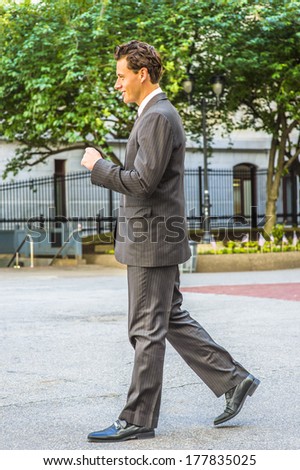 Wearing a black striped jacket, pants, tie, leather shoes,  a young businessman is walking outside an office building. / Businessman Walking