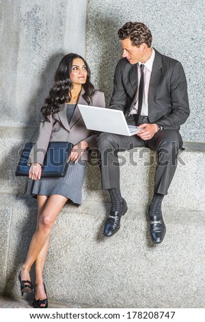 Dressing formally, standing or sitting, a young couple of business man and woman with a laptop computer, briefcase, are meeting outside, smiling, discussing, talking and working / Working Outside