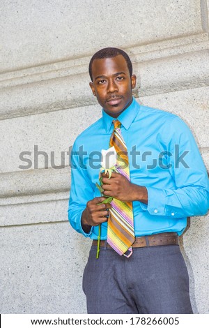 Dressing in a light blue shirt, colorful pattern tie, a young black guy is holding a white rose, standing by a wall, waiting for you. / Waiting for You