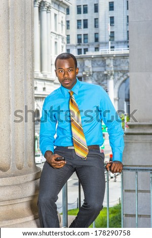 Dressing in a light blue shirt,  gray pants,  a pattern tie, a young black businessman is sitting outside an office building, holding a mobile phone, waiting for you. / Waiting Phone Call