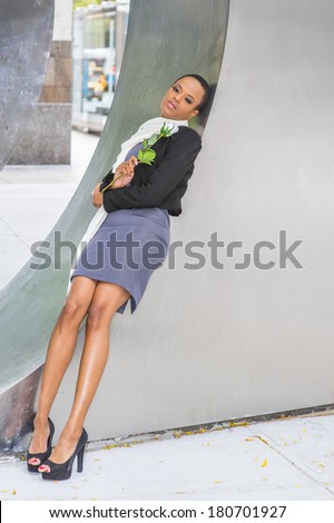 Pretty Black Woman with White Flower. Dressing in a woolen cropped jacket, dress, long scarf, high heels, holding a white rose,  a black fashion lady is relying on a metal structure, sad, thinking.