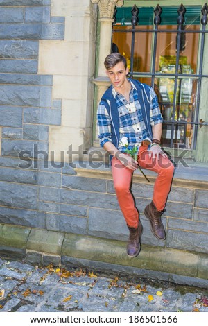 Young Man Holding White Rose. Dressing in a pattern shirt,  a hood vest,  red jeans, brown leather boot shoes, a young guy is sitting by a window, holding a white flower, waiting for you.