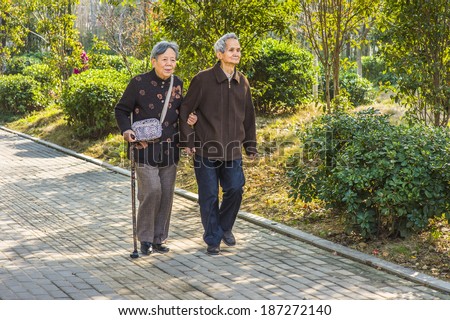 Senior Man and Woman Walking Outside. A  senior couple, 80 years old, helping each other, is walking outside, woman holding a walking stick.
