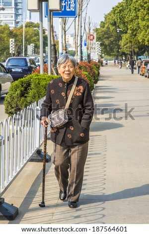 ANQING, CHINA - MARCH 21: Senior woman walks on street.  A 80 years old Chinese lady with a cane walks on the street on March 21, 2014.