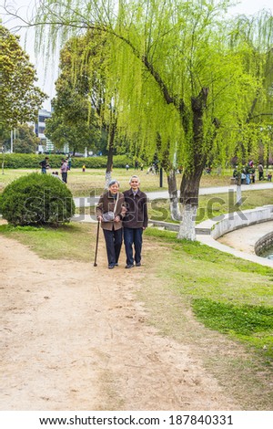 Senior Man and Woman Walking Outside. A  senior couple, 80 years old, helping each other, arm in arm,  is walking on a park, woman holding a walking stick.