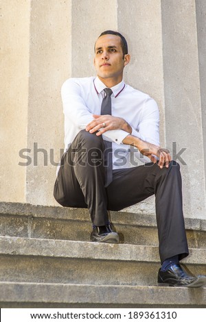 Man Thinking Outside.  Dressing in a white shirt, a black tie, pants, leather shoes, a young handsome guy is sitting on stairs outside an office building, taking a break and thinking.
