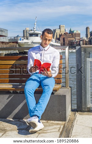 Man Reading Outside. Wearing a white shirt, blue pants, white sneakers, a young handsome guy is sitting on a chair under sunshine in a harbor, reading a  red book.