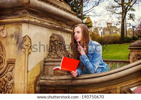 Girl Reading Outside . Wearing a Denim jacket, a young college student with long blond hair is reading a red book outside on the campus. Instagram Hefe effect.