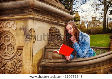 Girl Reading Outside . Wearing a Denim jacket, a young college student with long blond hair is reading a red book outside on the campus. Instagram Hefe effect.