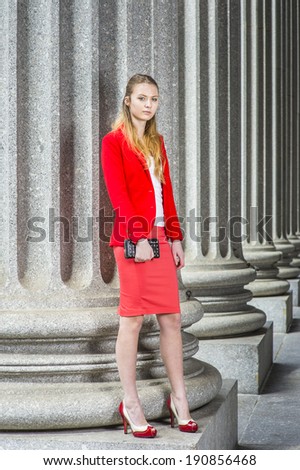 Fashion Girl. Dressing in a red blazer, white underwear, a red skirt, open toes high heels,  holding a small leather purse,  a female college student is standing by columns on campus.