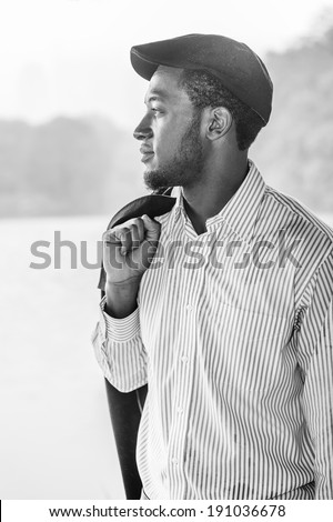Rainy Day, a little foggy, wet feel. Wearing a long sleeves shirt, a ivy cap, taking off a jacket on his shoulder,  a young handsome black man is standing by a foggy lake, confidently looking forward.