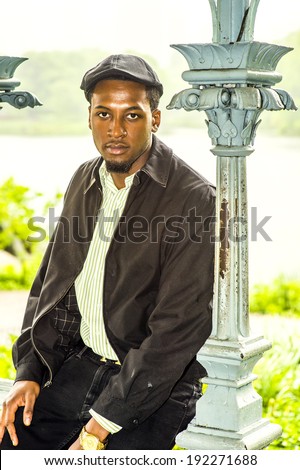 Rainy Day, a little foggy, wet feel. Dressing in a long sleeves shirt, a ivy cap,  a young handsome black man is sitting by a lake in a raining, foggy day, charmingly looking at you.