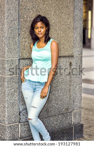 Girl Relaxing Outside. Wearing a green tank top, fashionable jeans, drop earrings, a young pretty black woman is standing by the wall, relaxing outside.
