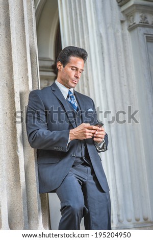 Man Texting Outside. Dressing in dark blue suit, necktie, a handsome, sexy, middle age businessman is standing outside office, looking down, texting on cell phone.