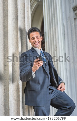 Man Texting Outside. Dressing in dark blue suit, necktie,  wristwatch, a handsome, sexy, middle age businessman is standing outside office, looking down, smiling, reading messages on cell phone.