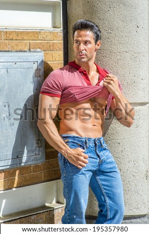 Strong Man. Holding on his shirt, a handsome, sexy, middle age guy is standing in the corner of the street, looking aside, confidently showing his success, hope, belief. Relaxing outside