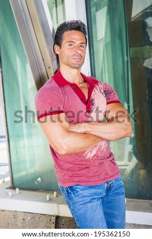 Portrait of Middle Age Man. Wearing a red Polo shirt, blue jeans, crossing arms, a handsome, sexy, middle age guy is leaning back against a metal structure, looking at you.