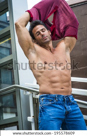Eyes closed, arms raised, a handsome, sexy, middle age man is taking off his shirt, showing his strong body.
