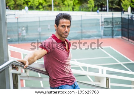 Man waiting for you. Wearing a red Polo shirt, blue jeans, stretching arms on the railing, a handsome, sexy, middle age guy is standing by a tennis court, passionately looking at you.