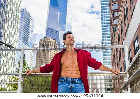 City Hunk.  Wearing a long sleeve red shirt, unbuttoned,  a handsome, strong, sexy, middle age guy is standing in the middle of high buildings, confidently looking forward.