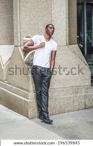 Street Fashion. Wearing a white V neck T shirt, pants, leather shoes, carrying a shoulder bag,  a young black college student is standing outside an office building, waiting, thinking